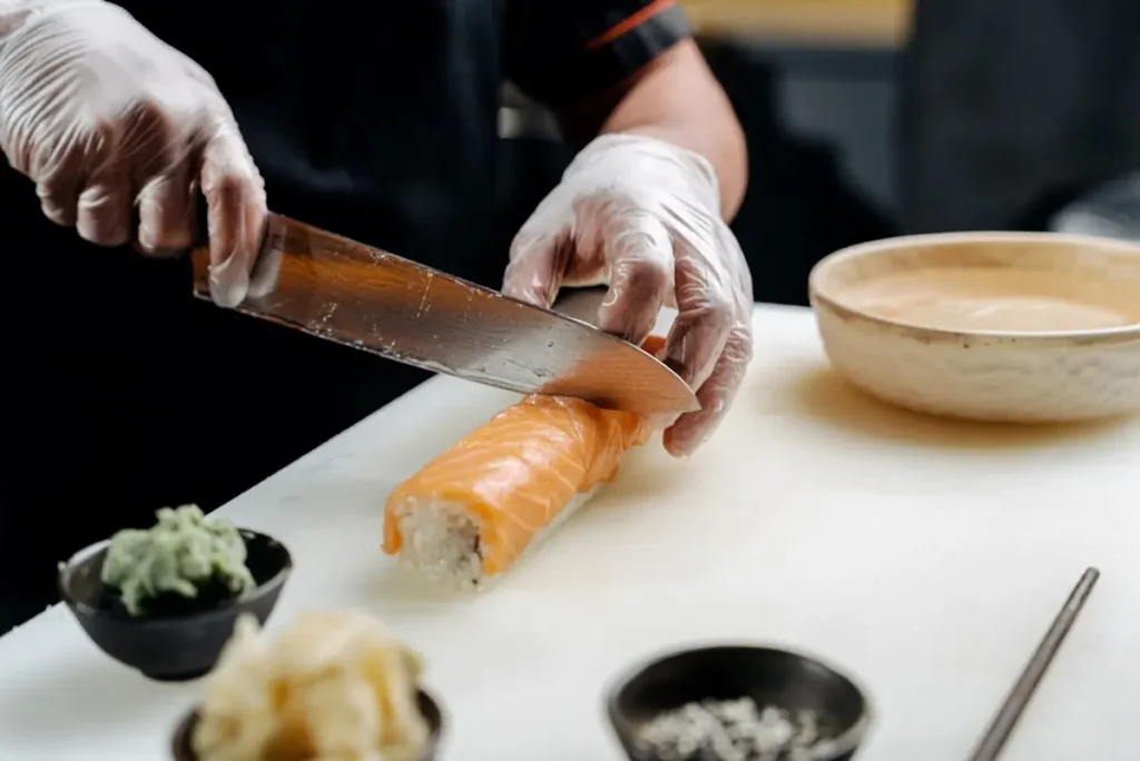 Como fazer sushi | Comidas Asiáticas Cozinheiro cortando um rolo de sushi com salmão usando uma faca afiada