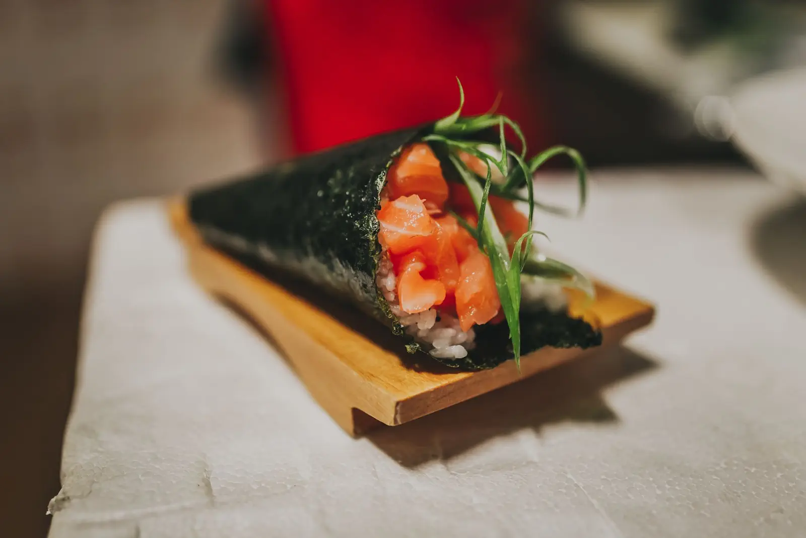 Temaki de salmão com arroz envolvido em alga nori sobre prato de madeira