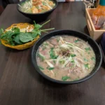 Tigela de pho bo com caldo de carne, macarrão de arroz, fatias de carne bovina e ervas frescas