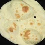 Naan: O que é e Como Fazer o Pão Indiano em Casa | Comidas Asiáticas: Pães naan assados com pontos dourados e tostados.