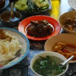 Mesa com arroz, travessas de curry birmanês e acompanhamentos de vegetais e sopa