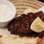 Chapli kebab paquistanês de carne moída achatada, servido sobre pão naan com limão e molho raita