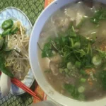 Tigela de khao piak sen do Laos com caldo, macarrão de arroz grosso e guarnições